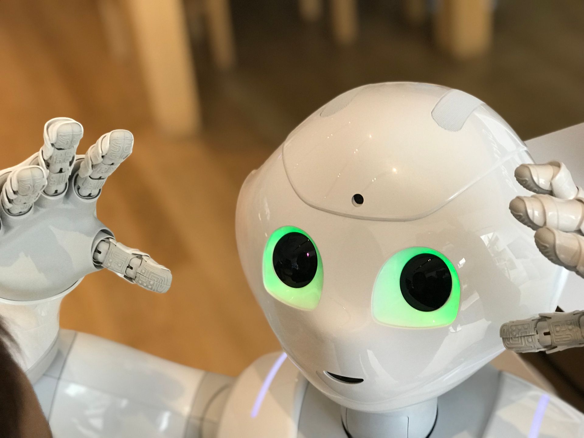 Robot with glowing green eyes raising its splayed hands in an expressive, surprised, and defensive pose.